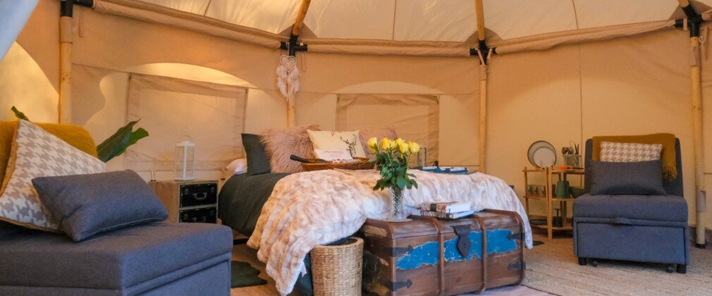 Inside a bell tent with beds chairs and flowers