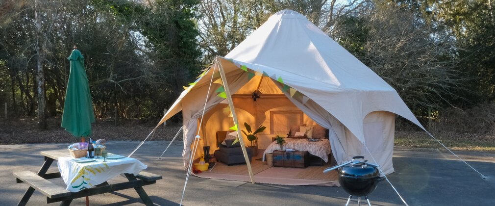 Bell tent furnished with cosy bedding with picnic bench and barbeque outside the tent