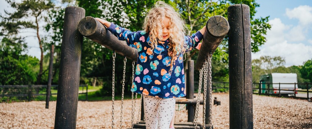 Girl playing on wooden play equipement at Camping New Forest campsite