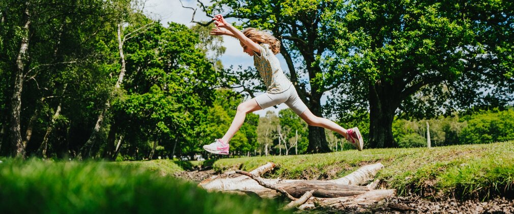 Girl jumping over a stream at New Forest campsite