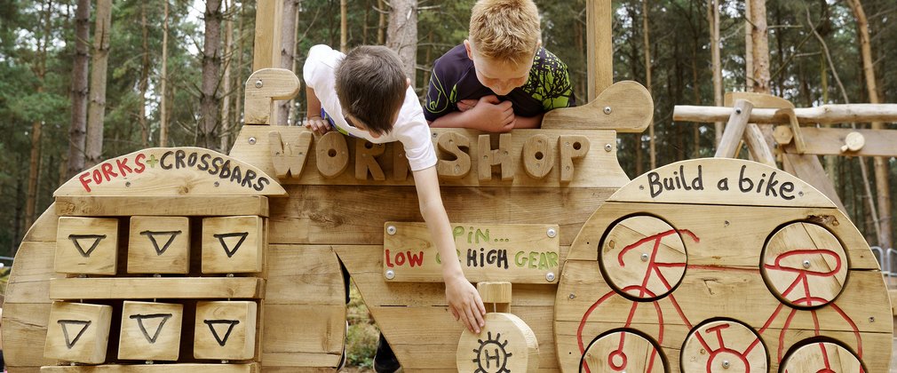 Boys playing on a wooden piece of play equipment shaped like a bike