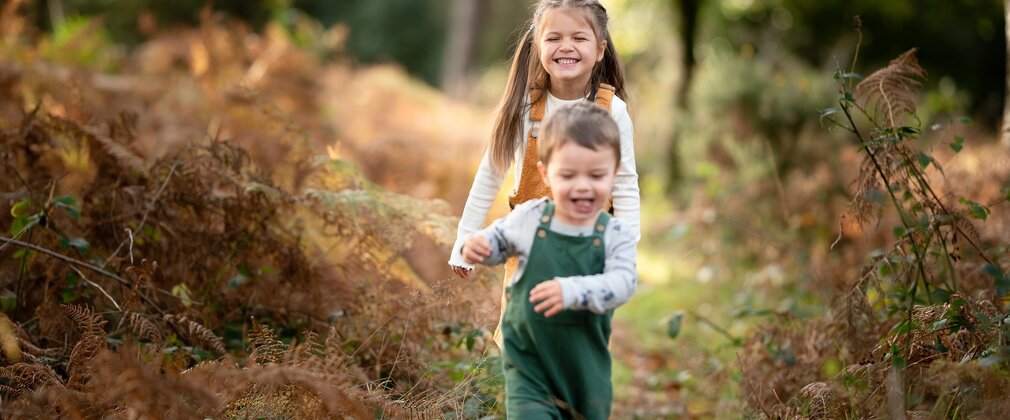 A young girl and boy on a grassy track surrounded by autumnal foliage.