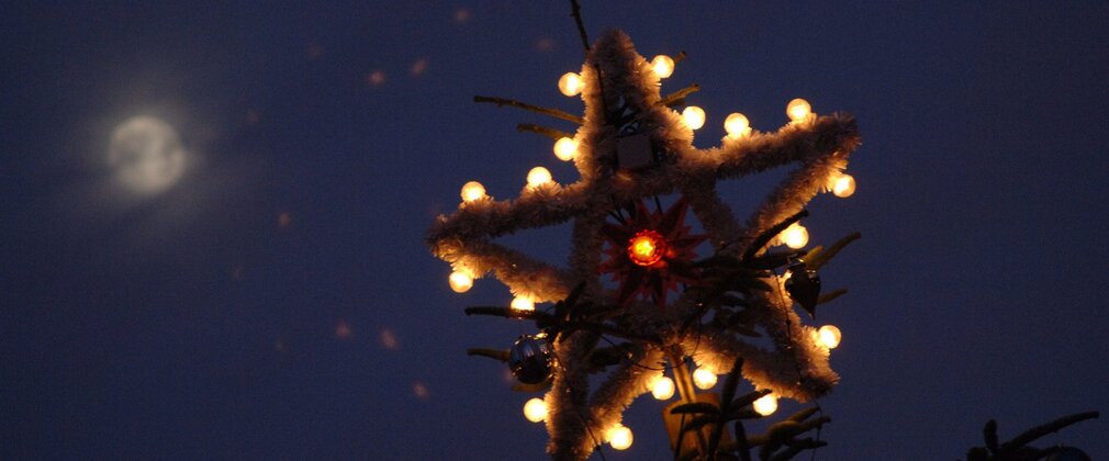 Close-up of star on top of an outdoor Christmas tree, with lights.