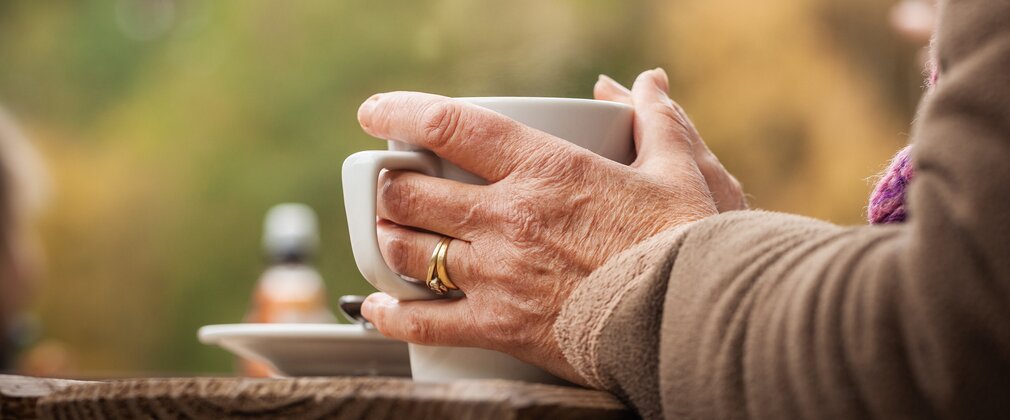 Close-up of a mug being held between two hands on a picnic bench outside.