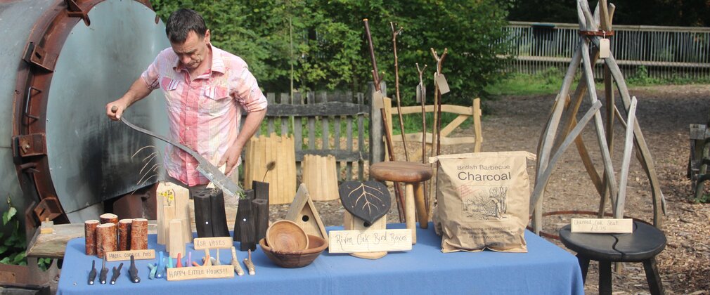 A man stands behind a table covered in a blue table cloth full of coppiced products ready to sell.