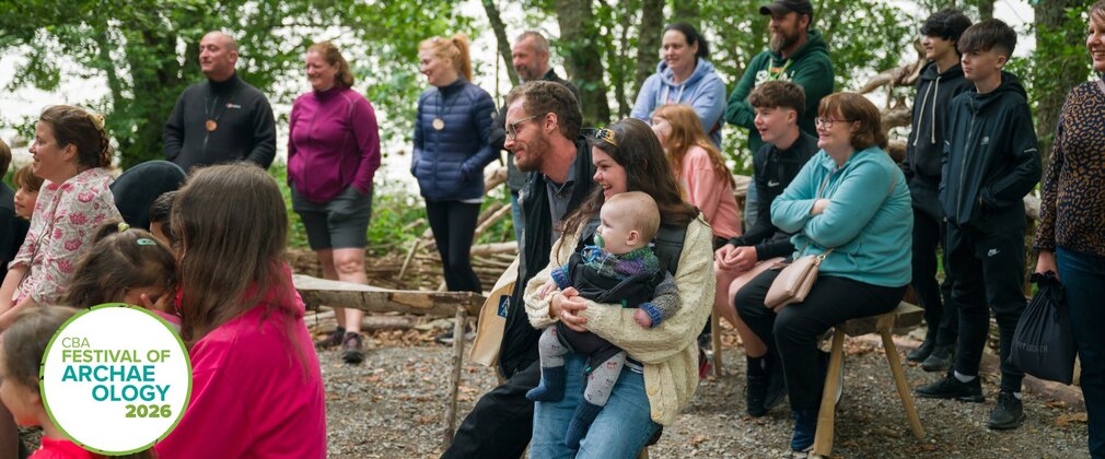 Spectators sit round watching a demonstration that can't be seen with smiles on their faces. 