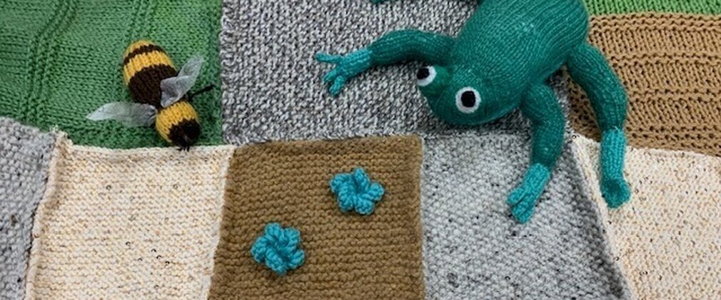 A crochet blanket with a crochet bee, crochet flowers and a crochet frog sat on top.
