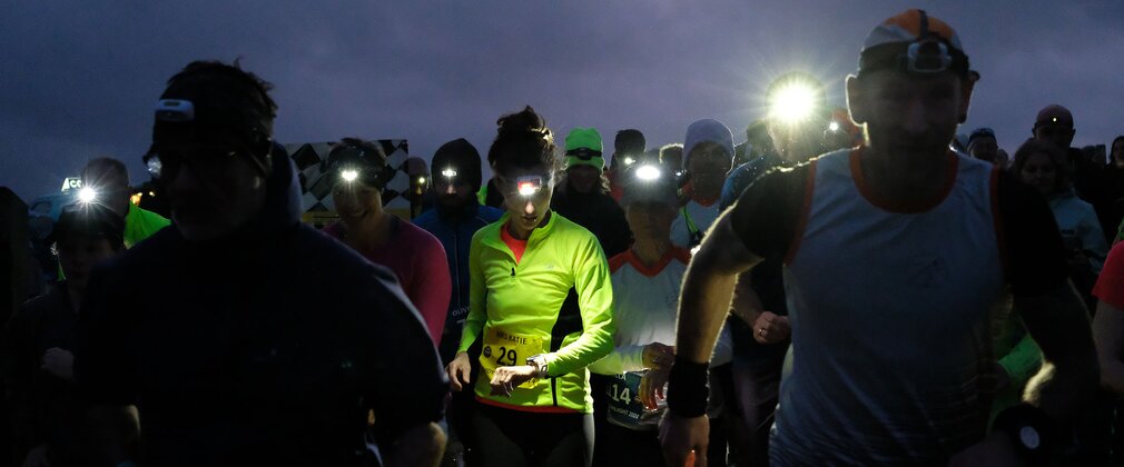 Night runners wearing head torches. The central figure is checking their watch.