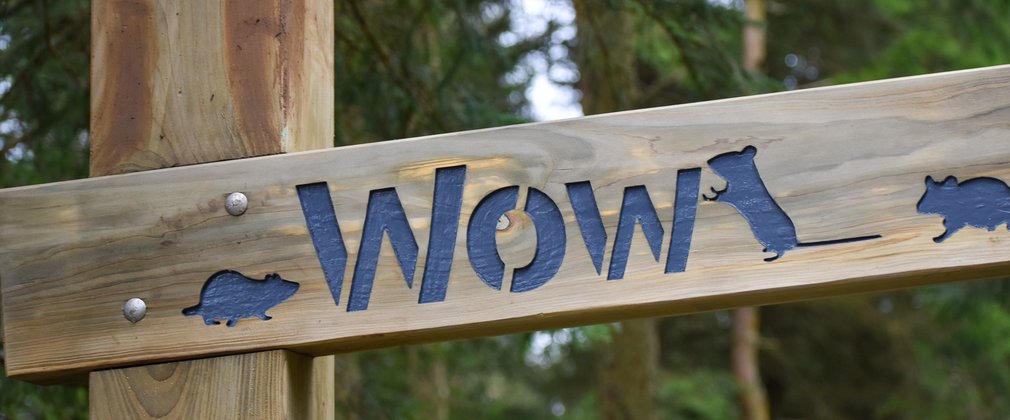 A wooden archway structure with the word Wow engraved on it with pictures of mice 