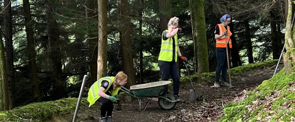 Four women wearing high visibility vests helping maintain a mountain bike trail in a woodland.