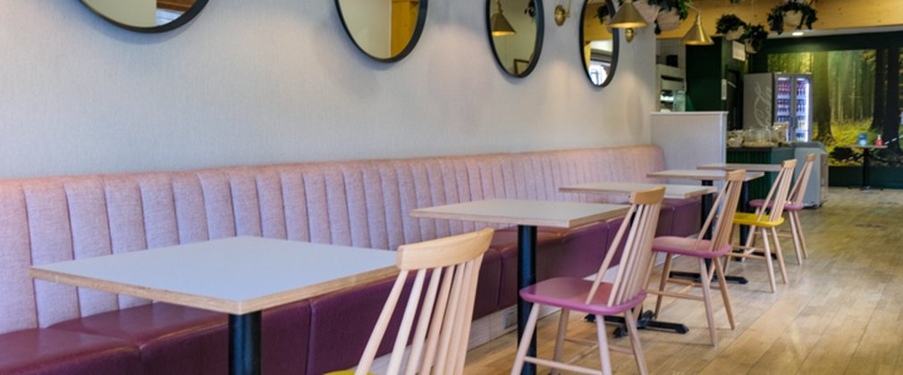 A cafe with pink bench seating and yellow and pink chairs
