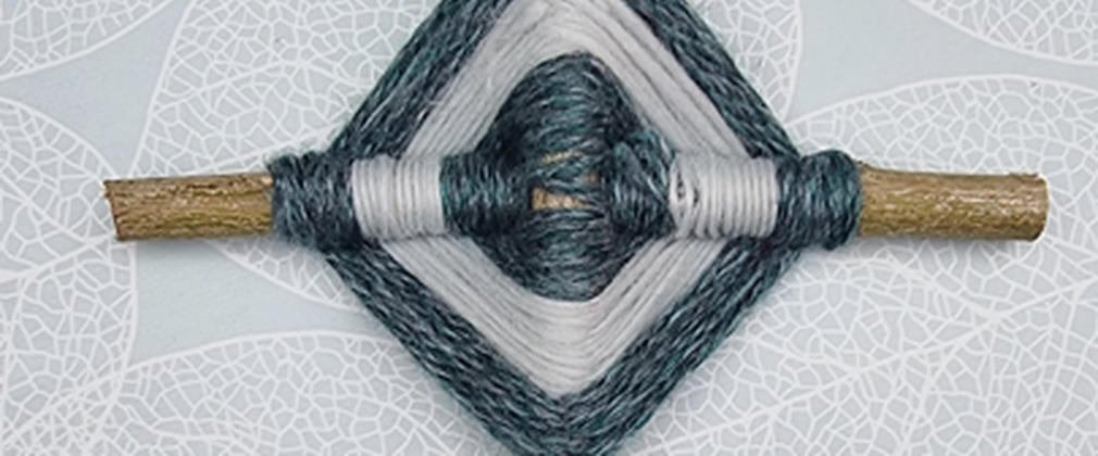 A woven dreamcatcher made from white and blue string wrapped around crossed over sticks