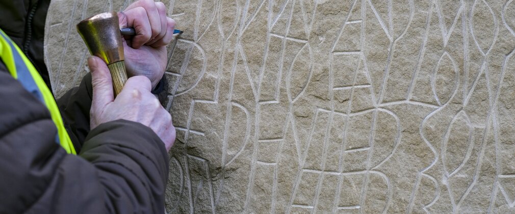 A stone carver using a chisel to create letters in stone