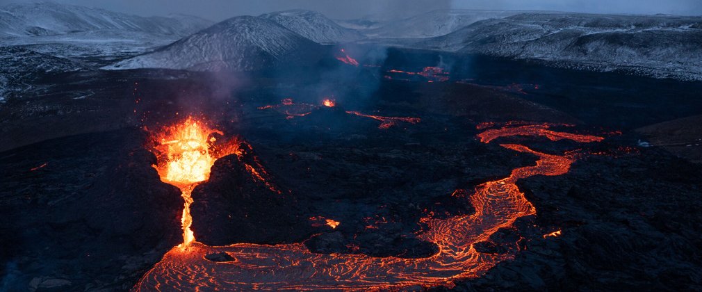 Lava pouring from a volcano with snowy mountains behind