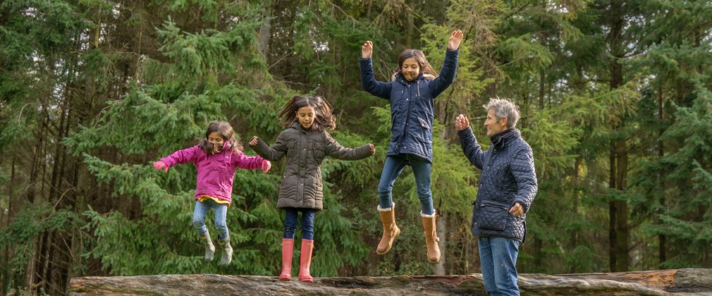 Children jumping off a tree trunk in the forest
