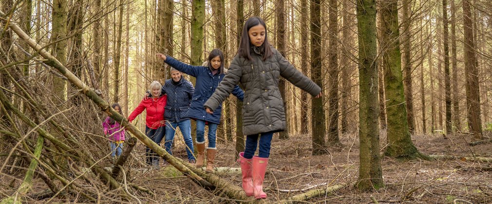 Children walking along a log in the forest