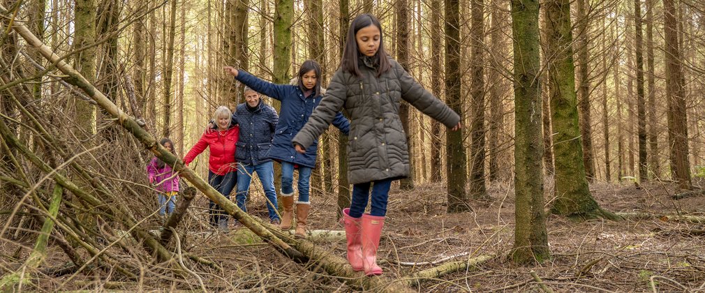 Children walking along a log in the forest