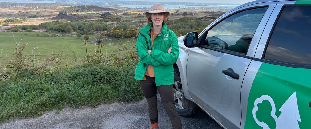 A woman standing outdoors by a Forestry England car.