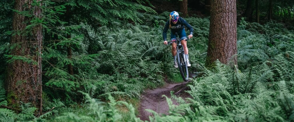 A female cyclist in sports gear and helmet riding downhill on a forest path