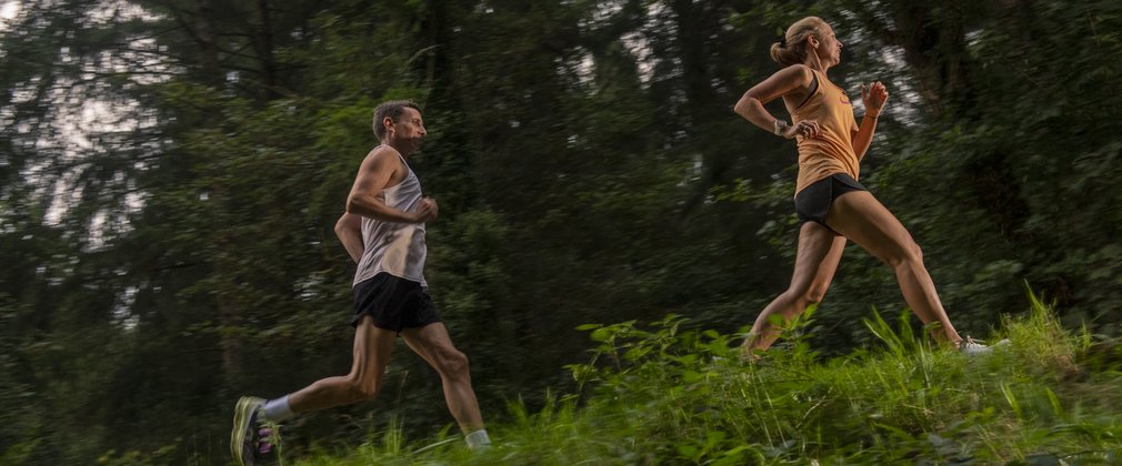 A couple running up a hill with trees in the background