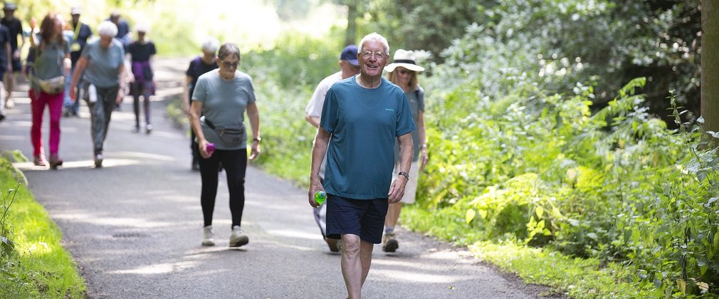 A group of people wearing active wear are walking on a path through the forest
