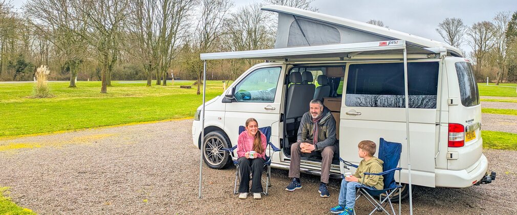Family sitting outside their campervan on a hardstanding plot at Fineshade campsite in February