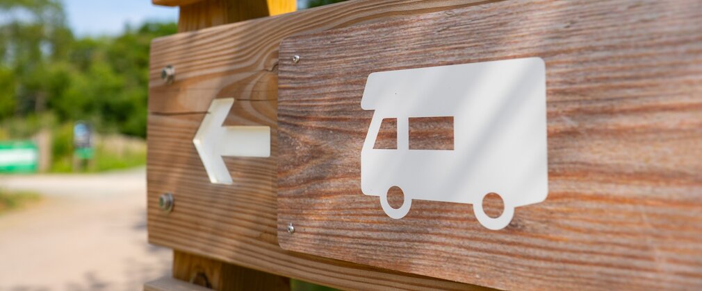 Wooden signs with a motorhome symbol and an arrow indicating the direction to travel in