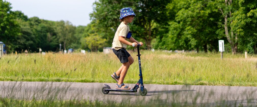 Boy in a sun hat riding a scooter along a path with trees in the background