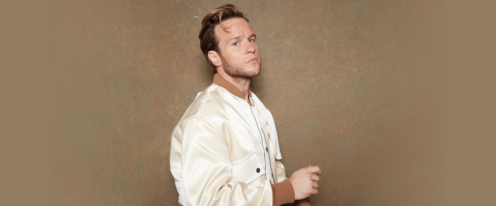 Olly Murs standing against a beige background