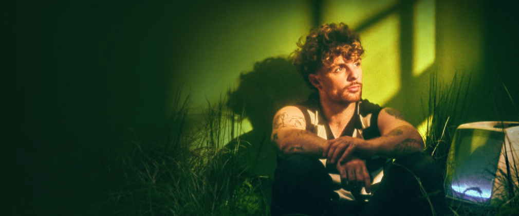 Singer Tom Grennan sitting down looking off into the distance