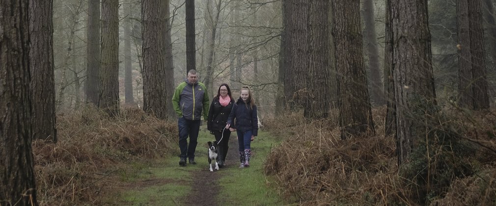 Man, woman and girl walking the dog through pine trees