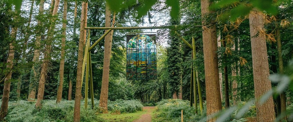 A decorated stained glass pane hangs over a forest path.