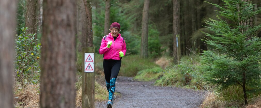 A woman in running clothes and a pink hat running along a forest path in winter