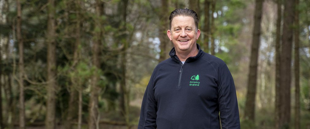 Man in forestry england uniform standing in a forest smiling