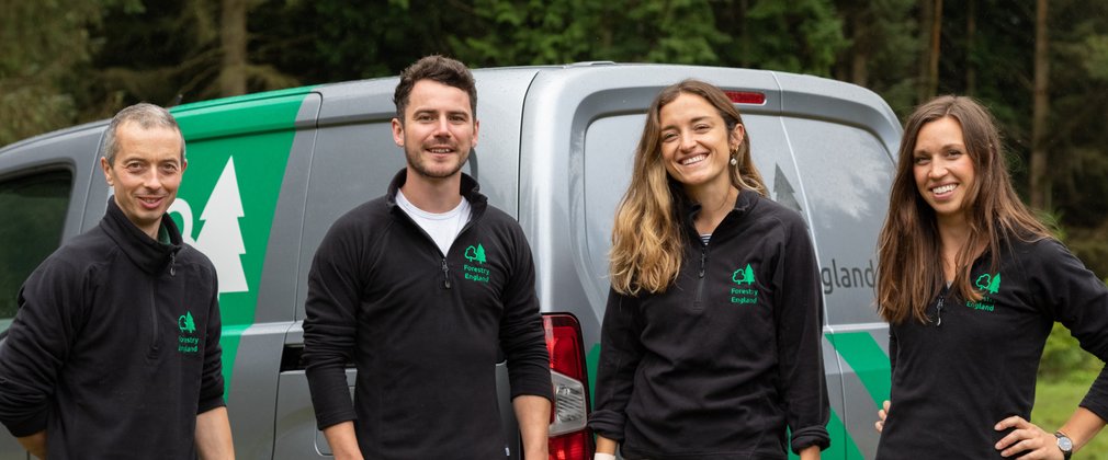 Group of Forestry England staff stood smiling in front of grey Forestry England van