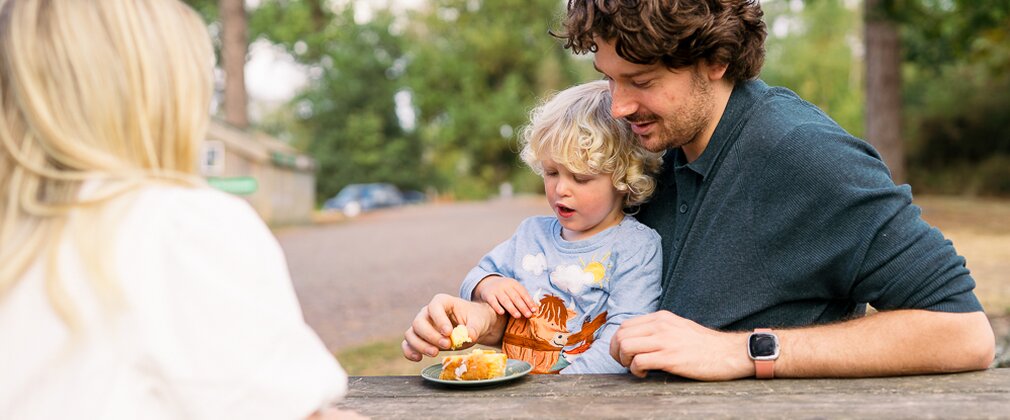 A young boy eating some cake on a bench with his family