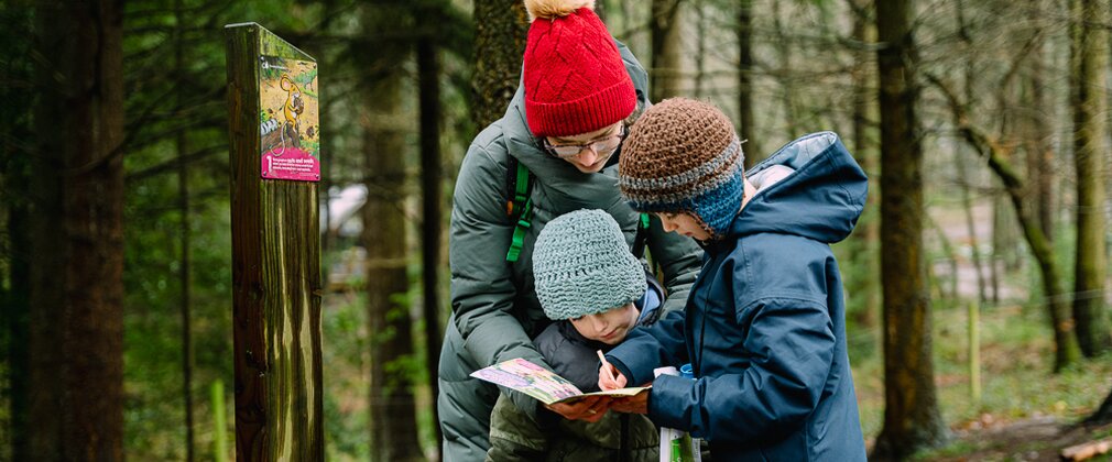 A mother and her two children filling out the Gruffalo orienteering leaflet next to a Gruffalo orienteering post