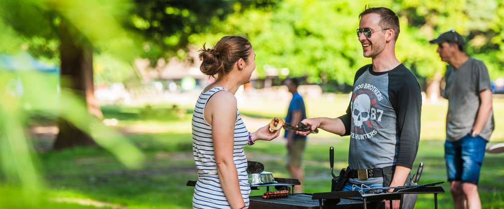 Man hands woman sausage at BBQ