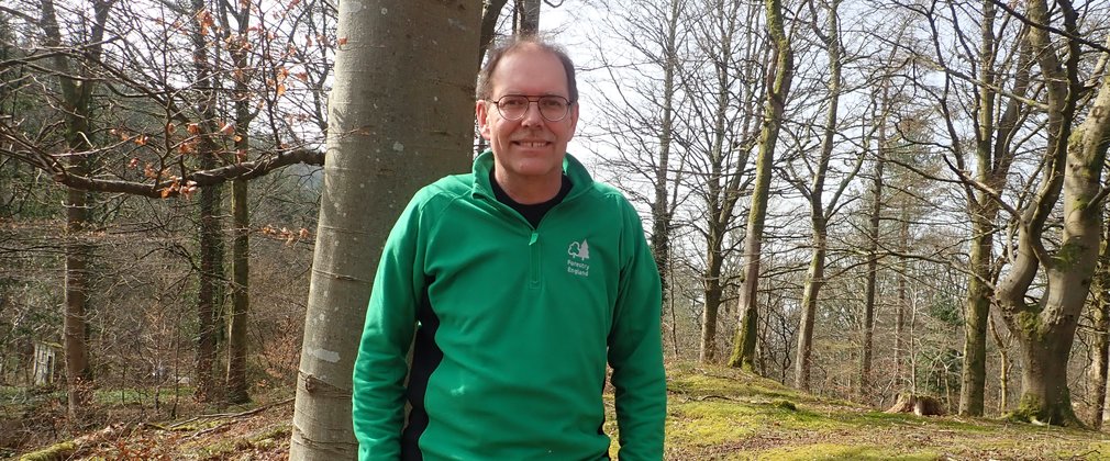 Member of staff in Forestry England uniform stood by a tree