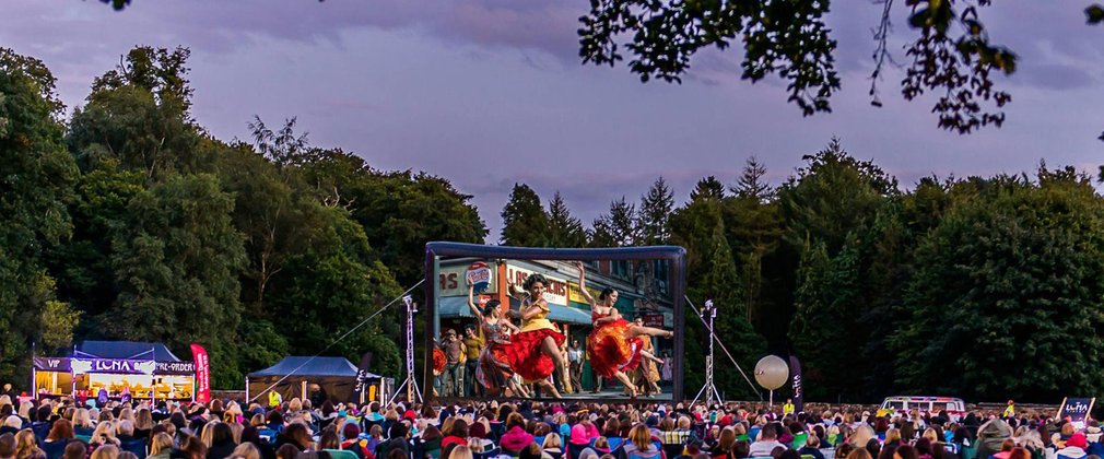 A crowd gather in the forest to watch an outdoor cinema screening of West Side Story