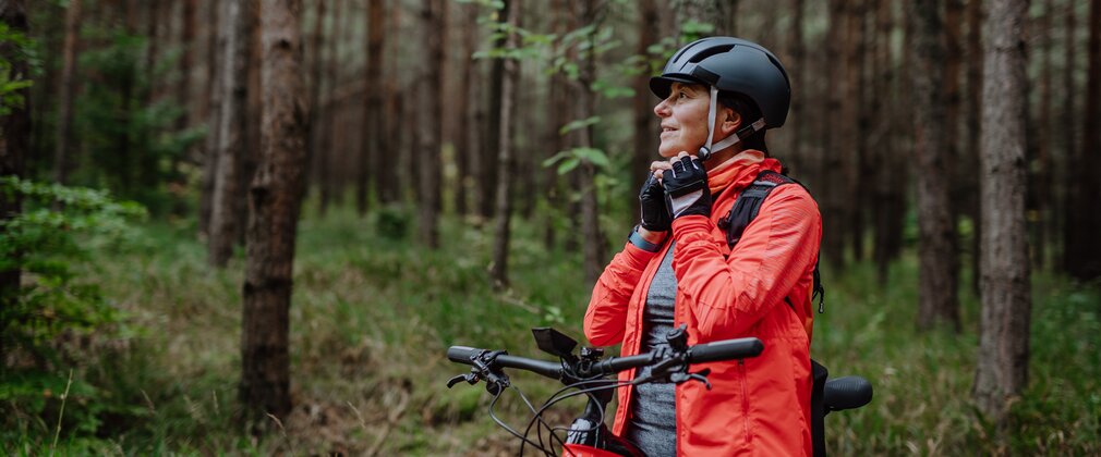 Woman biker putting on cycling helmet in forest