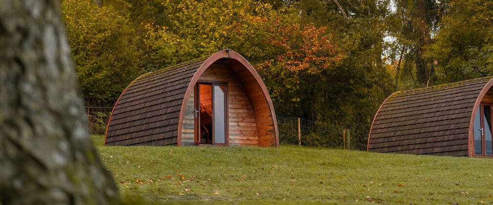 Arched wooden camping pods next to autumn trees.