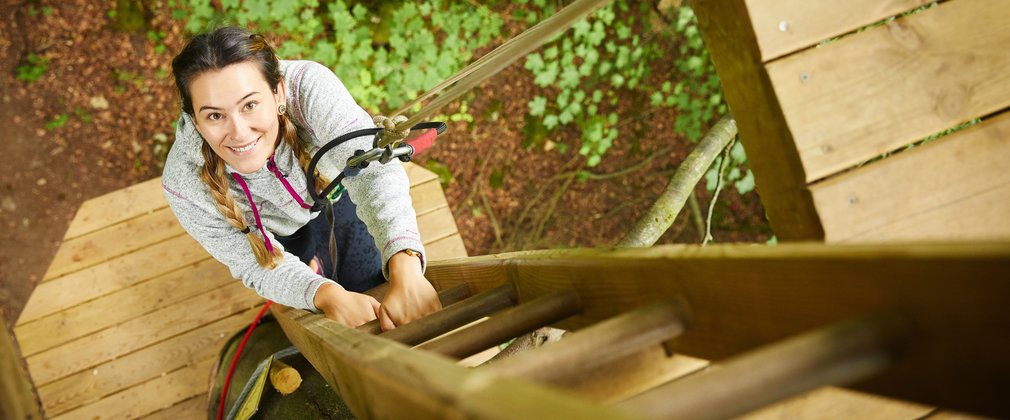 A person attached by rope climbing a ladder on a tree
