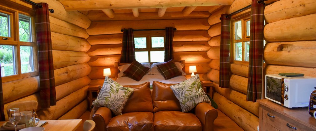 Interior of a rustic log cabin with bed, sofa and dining/kitchen area visible