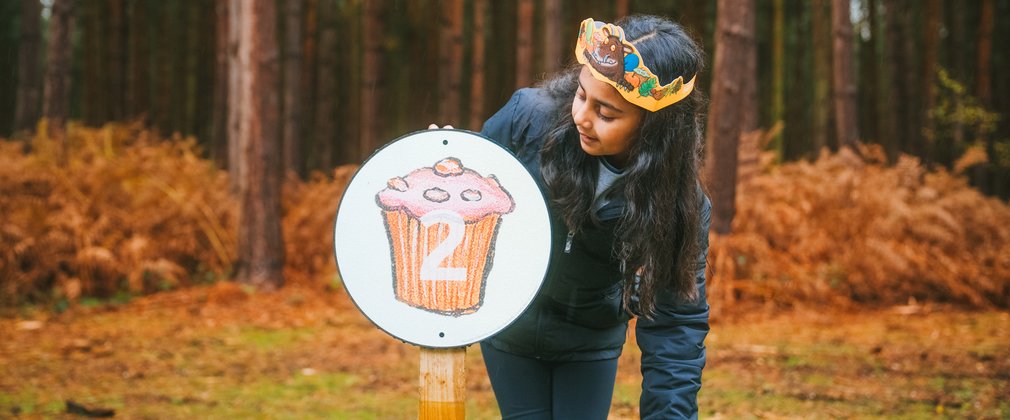 Girl in forest pointing at cupcake panel