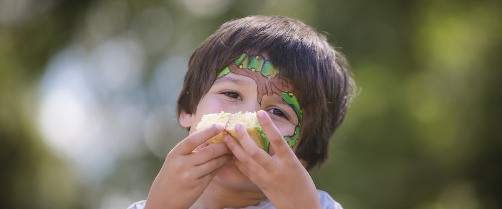 Boy with Gruffalo face paint eating a piece of cake