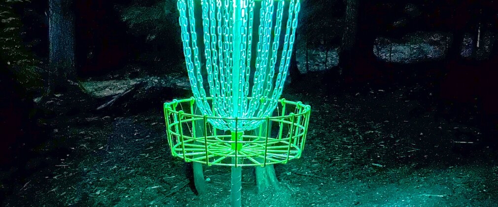 A disc golf basket in the dark lit up with neon blue light