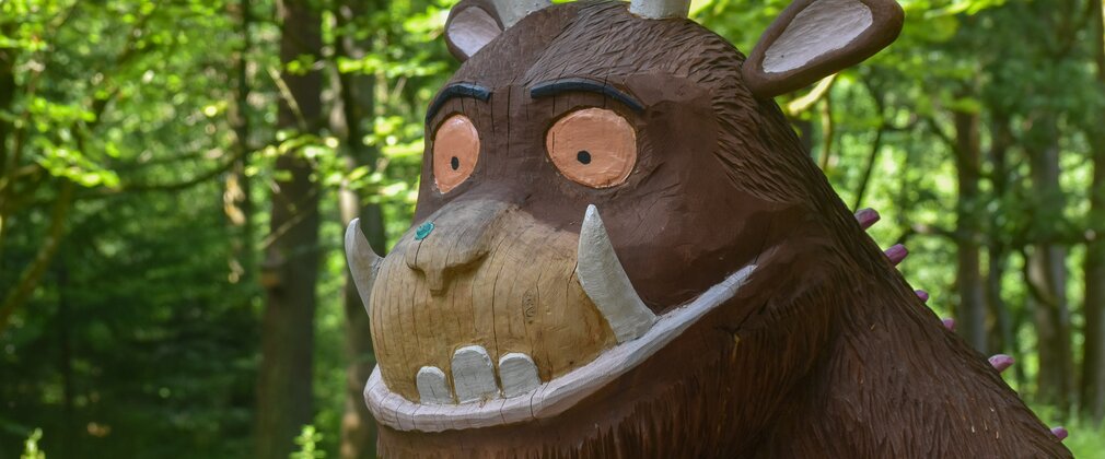 A headshot of a wooden Gruffalo sculpture in a forest