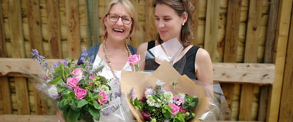 2 women hold bouquets flowers they have arranged. They look happy with their arrangements.