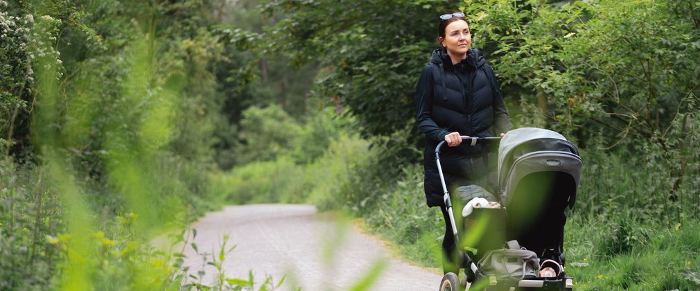 A woman pushing a pram along a trail in a forest